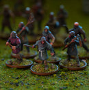 A group of painted tabletop wargaming miniatures representing soldiers in medieval-style armor and cloaks, standing on textured green bases with a blurred background of more figures.