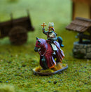 Miniature figure of a knight on horseback with a cross, set against a blurred natural background.