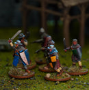 A group of painted fantasy warrior miniatures on round bases, posed on a textured green tabletop with a blurred wooden structure in the background.