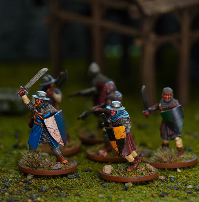 A group of painted fantasy warrior miniatures on round bases, posed on a textured green tabletop with a blurred wooden structure in the background.