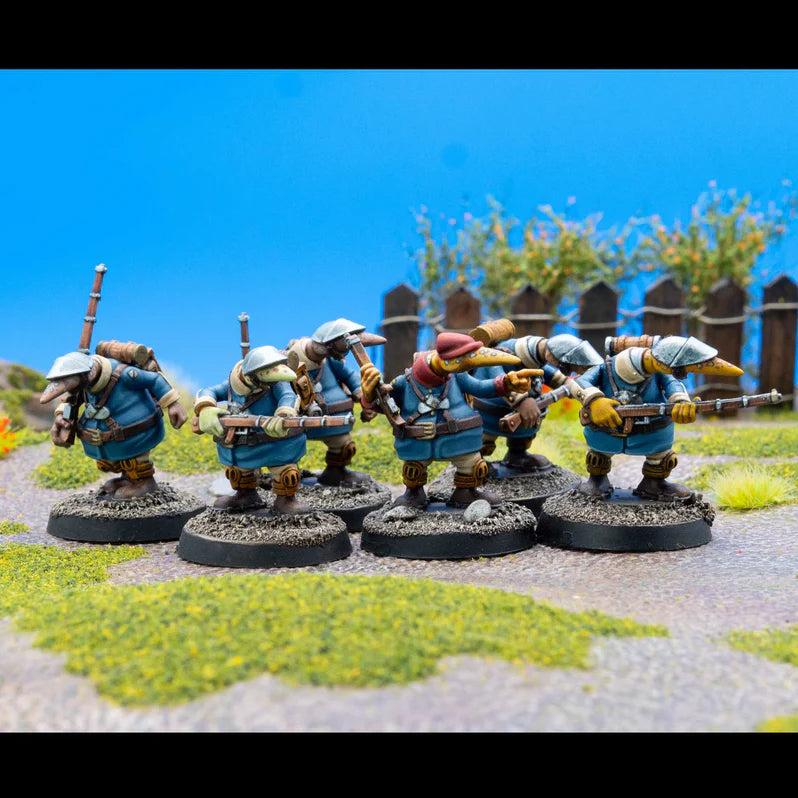 Five miniature figures in blue uniforms with rifles on a grassy area with a wooden fence and blue sky in the background.