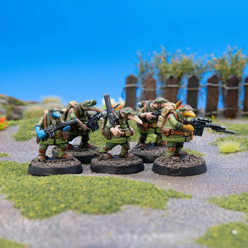 Four miniature figures in green uniforms with weapons on a textured surface with grass and wooden fence in the background.