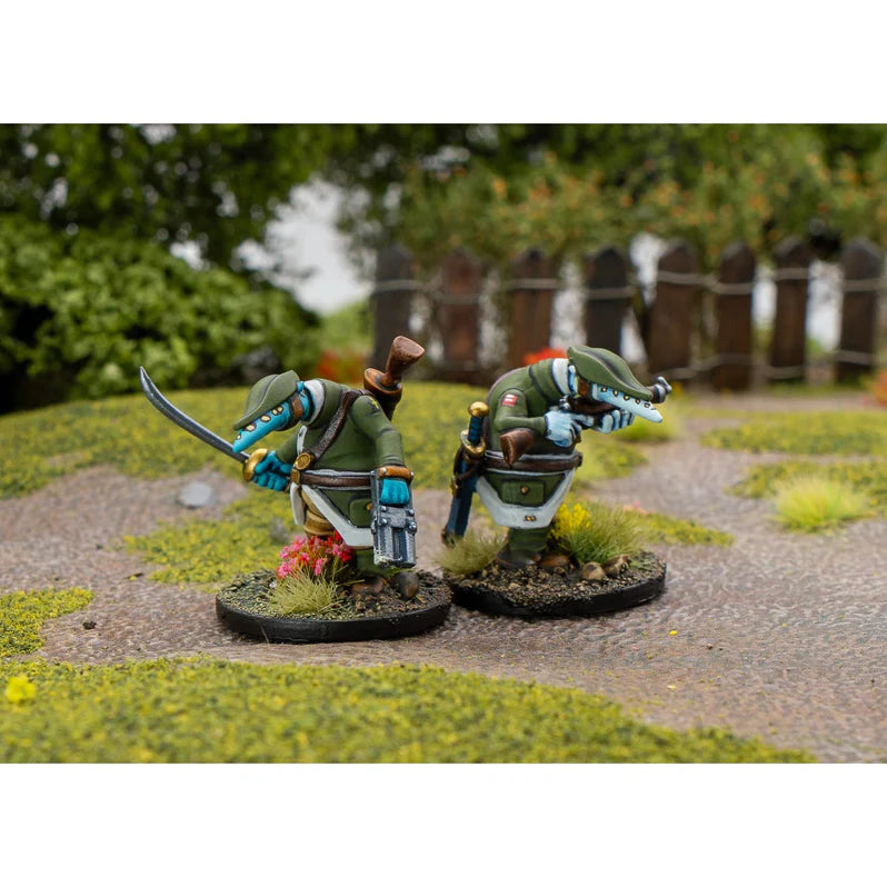 Two miniature figures on a garden path with greenery and a wooden fence in the background.