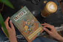 Person holding a 'Root' core book on a table with a cup of coffee.