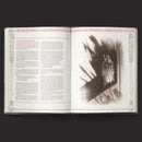 Open book with text on one page and a black and white photograph of a figure on the other, against a dark background.